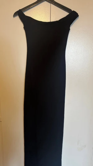 Svart offshoulder långklänning - En elegant svart långklänning med offshoulder-design. Klänningen har en smal passform och är perfekt för dig som gillar en stilren och tidlös look. Använd en gång 