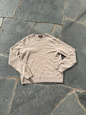 Beige stickad tröja från Uniqlo - En stilren beige stickad tröja från Uniqlo med rund halsringning och långa ärmar. Tröjan har ribbade muddar vid ärmslut och nederkant. Perfekt för lager på lager och enkel att matcha med olika outfits.