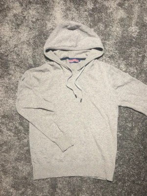 Grå hoodie från William de Faye - Snygg grå hoodie från William de Faye med klassisk huva och dragsko. Tillverkad i mjukt kashmere material som känns skönt mot huden. Perfekt för en avslappnad och stilren look. Långa ärmar och ribbade muddar ger en clean finish.