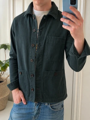 Mörkgrön overshirt från Dobber - Stilren mörkgrön overshirt från Dobber med klassisk krage, tre stora utanpåfickor och knäppning framtill. Tillverkad i ett slitstarkt bomullstyg som ger en avslappnad men snygg look. Perfekt att bära över en t-shirt för en casual vibe.