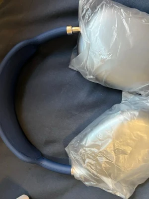 Blå Apple AirPods Max hörlurar - Snygga over-ear hörlurar från Apple i en stilren blå färg. De har en vadderad bygel och öronkåpor i aluminium med mjuka kuddar för extra komfort. Perfekta för dig som vill ha grymt ljud och modern design.