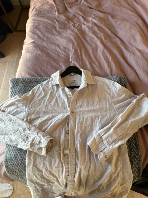 Beige linneskjorta från Jack & Jones - Säljer en beige skjorta från  Essentials, tillverkad i svalt linne. Skjortan har klassisk krage, långa ärmar och knappar framtill. Den är aldrig använd så är i nyskick, storlek M