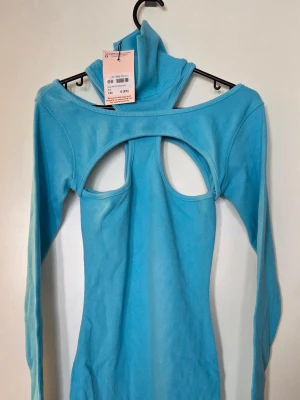 Blå ribbad klänning med cut out - Trendig blå ribbad klänning med lång ärm och unik cut out-detalj över bröstet. Klänningen är kroppsnära och har en kort längd, perfekt för dig som vill sticka ut. Materialet är mjukt och stretchigt, vilket ger en bekväm passform.