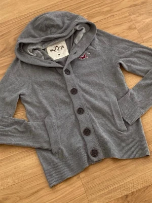Hollister Cardigan  - Säljer en riktig snygg Hollister Cardigan, denna är väldigt välkänd. Skicket är 10/10. Priset kommer ligga på 599kr men kan sänkas. Storlek M.