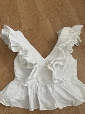 Söt, Vit volang topp 💕 - Supersöt vit topp med smockad midja och breda volangdetaljer längs axlar och nederkant. Toppen är ärmlös och har en dragkedja i bak för enkel påklädning!💗 egentligen storlek 38 men insydd lite på sidorna så skulle säga bara en storlek mindre 💕💗