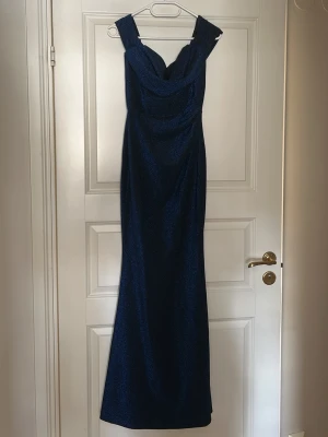 Marinblå glittrig långklänning - Säljer min marinblå balklänning med glittrigt tyg och breda axelband. Kan bäras som off shoulder eller med axelbanden uppe på axlarna. Klänningen har en draperad urringning och figurnära passform. Verkligen så fin klänning!😍Jag är 163 och den nuddar marken!