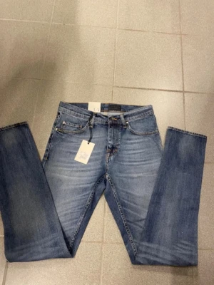 Blå raka jeans med tvättad look från tiger of sweden - Snygga blå jeans med rak passform och klassisk femficksdesign. Jeansen har en tvättad look med ljusare partier och detaljerade sömmar. Tillverkade i denim med en skinnpatch bak i midjan. Perfekta för en avslappnad stil.