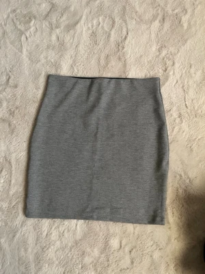 Grå kortkjol från Cubus i storlek XS - Snygg och enkel grå kortkjol från Cubus i storlek XS. Kjolen har en rak och tight passform och är tillverkad i ett mjukt material som känns bekvämt mot huden.