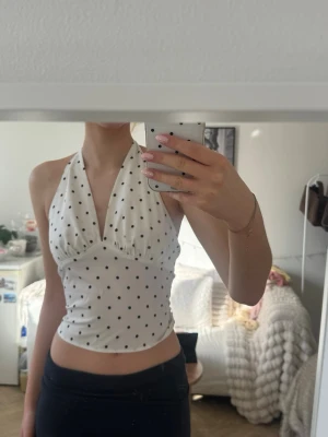 Polka dot  halterneck topp - Snygg vit halterneck topp med svarta prickar och djup v-ringning. Toppen är croppad och har en figurnära passform, perfekt för att skapa en trendig look. Köpt på marknad i Sevilla för halvår sedan💞