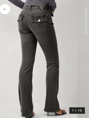 TRUE Religion BECCA MID RISE BOOT CUT FLAP stl W27 L32 - Jeans från True Religion med de ikoniska bakfickorna. Färgen är charcoal .Bootcut Femficksdesign. Jeansen har varit upplagda ca 6 cm och har tecken på detta samt ett hål längst ner på ena benslutet. se bilder. För övrigt bra skick.