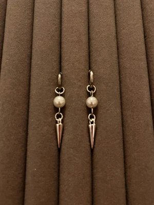 Silvriga sopformade örhängen med pärla - Säljer ett par stilrena örhängen i silverfärg med små vita pärlor och spetsiga hängande detaljer. Örhängena har en modern design med rund pärla och metallisk konformad pendel. Perfekta för dig either vill ha något unikt och trendigt.