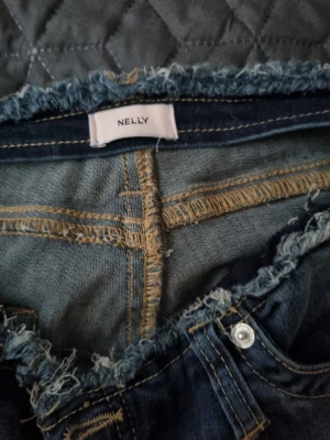Blåa vida jeans från Nelly - Säljer ett par blåa jeans från Nelly med råa, fransiga kanter i midja och benslut. Jeansen har en avslappnad, vid passform och klassiska bakfickor. Perfekta för en trendig och avslappnad stil. Använd fåtal gånger storlek 42 men passar 40 också. 