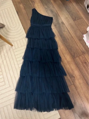 Marinblå långklänning från Beauut - Säljer en marinblå långklänning från Beauut med ett lager på lager-tyll och oneshoulder-design. Klänningen nån fläck som jag märkte efter jag fick hem den men de borde gå att få bort🥰köpt på plick