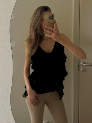 Svart volang linnetopp med tunna axelband - Säljer ett svart linne från Zara med tunna axelband och fina volanger. Toppen har en luftig passform och materialet är lätt och transparent, vilket ger en fin effekt. Använt några få gånger så skicket är väldigt bra!