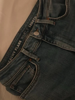 Blå Peachy Flare jeans - Snygga blå jeans från Peachy med flare-modell. Jeansen har klassisk femficksdesign, knappgylf och markerade sömmar. Perfekta för dig som gillar en trendig och avslappnad stil.