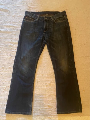 Mörkblå redwood bootcut jeans - Säljer ett par mörkblå bootcut jeans med klassisk femficksdesign och lätt slitna detaljer framtill. Jeansen har normal midja och raka ben som går ut något nedtill. Tillverkade i denim med snygg tvättad look.