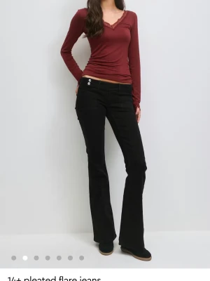 Svarta utsvängda jeans - Säljer ett par svarta jeans med utsvängda ben och snygga detaljer på bakfickorna. Jeansen har låg midja, knapp- och femficksdesign.