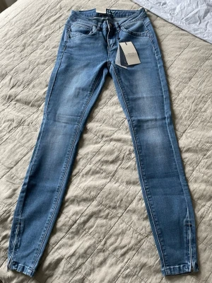 Blå skinny jeans från Only - Snygga ljusblå skinny jeans från Only med dragkedjor vid bensluten och klassisk femficksdesign. Jeansen har en smal passform och är tillverkade i stretchigt denim för extra komfort. Perfekta för en trendig och avslappnad look.