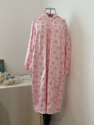 Rosa blommigt nattlinne med spets - Sött rosa nattlinne med blommönster och vita spetsdetaljer vid krage och bröst. Har ingen ettikett som visar märke. Tillverkad i Frankrike. Materialet syns i sista bild. One size.
