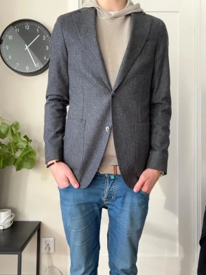 Oscar Jacobson kavaj  - Stilren och snygg kavaj/blazer i ullmaterial ifrån Oscar Jacobson i storlek 50, vilket motsvarar M. Väldigt fint skick och använd max 4-5 gånger. Funkar lika bra med skjorta under samt med hoodie för en mer slapp stil. Köpt i butik för 5299kr. Säljer då den tyvärr inte kommer till användning. Mvh Ville 