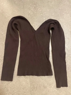 Brun ribbad topp från H&M - Mörkbrun ribbad topp från H&M med v-ringad hals, off shoulder och långa ärmar. Sitter tight och har en stretchig passform som framhäver figuren. Perfekt att styla med jeans eller kjol för en trendig look. Kan mötas upp i Stockholm.