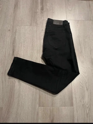 Tiger of Sweden - Svarta slim fit jeans med klassisk femficksdesign och diskreta sömmar. Jeansen har en läderpatch vid linningen och är tillverkade i ett stretchigt denimtyg som ger en snygg passform.