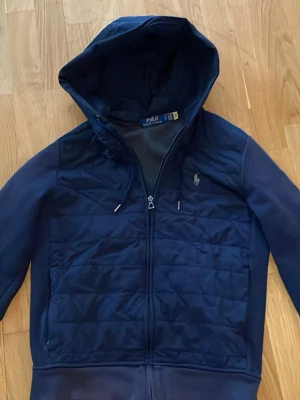 Polo Ralph lauren cardigan  - Snygg mörkblå cardigan från Polo Ralph Lauren med dragkedja och quiltad front. Klassisk huva och broderad logga på bröstet. Perfekt inför våren!! Sick 8/10 finns en enstaka defekt som man inte lägger märke till.