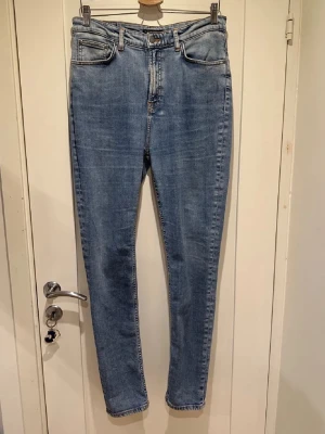 Nudie Jeans - Säljer ett par klassiska blå skinny jeans från Nudie Jeans. Jeansen har fem fickor, normalhög midja och smal passform hela vägen ner. Tillverkade i denim med snygga slitningar och Nudie Jeans signaturbroderi på bakfickorna.