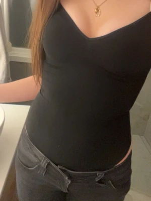 Svart body med v-ringning från H&M  - Säljer en svart body med v-ringning och breda axelband. Sitter tight och har en slät, figurnära passform. Materialet är stretchigt och bekvämt, perfekt att bära under kläder eller som den är. Enkel och stilren design utan synliga detaljer. Den är köpt samma dag som den var upplagd på plick därför vill jag sälja den