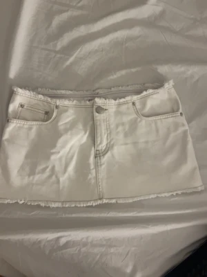 Vit jeanskjol med råa kanter - Snygg vit kort jeanskjol med råa kanter och klassiska fickor både fram och bak. Kjolen har knapp- och dragkedjestängning framtill och är perfekt för en trendig och avslappnad look. Passar till allt från sneakers till boots.