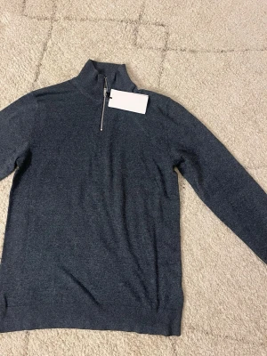 Mörkblå halvzip  - Mörkblå stickad tröja med halvzip från Lindbergh i storlek S. Tröjan har långa ärmar och ribbade muddar vid ärmslut och nederkant. Perfekt för lager-på-lager och snygg till jeans eller chinos. Nypris 599kr. 