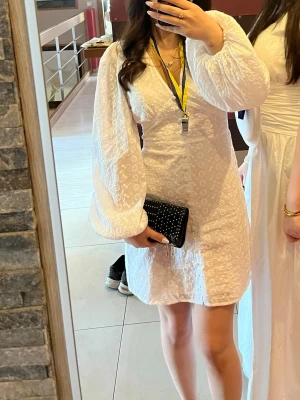 Vit kort klänning med broderad spets - Säljer en vit kort klänning med v-ringning och långa puffärmar. Klänningen har ett broderat spetsmönster och är tillverkad i bomull. Perfekt för studenten. Jag har haft på mig den bara på studentdagen. 