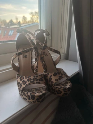 Leopardmönstrade klackskor  - Snygga pumps med leopardmönster och hög platåklack. Skorna har korsade remmar över foten och justerbar ankelrem med spänne. Köpta i en fin butik i USA och säljs inte längre 