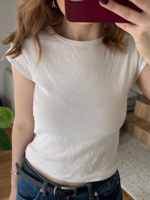 Vit ribbad T-shirt topp från Zara  - Säljer en vit ribbad topp med korta ärmar och rund halsringning. Perfekt att matcha med jeans eller kjol för en enkel och clean look. Materialet är mjukt och stretchigt, vilket gör den bekväm att bära hela dagen.