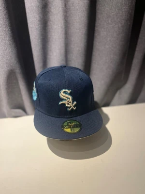 Mörkblå White Sox keps New Era - Snygg mörkblå keps från New Era med White Sox-logga broderad framtill i vitt och ljusblått. Klassisk 59FIFTY-modell med platt skärm och officiell sticker kvar på skärmen. Extra brodyr i ljusblått på sidan för unik look.    Storlek 7 1/8 