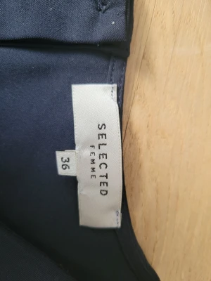 Mörkblå blus från Selected Femme - Snygg mörkblå blus från Selected Femme i storlek 36. Blusen har långa ärmar, knappar i ryggen och en lätt utsvängd nederkant som ger en fin siluett. Materialet känns mjukt och följsamt, perfekt för en stilren look.