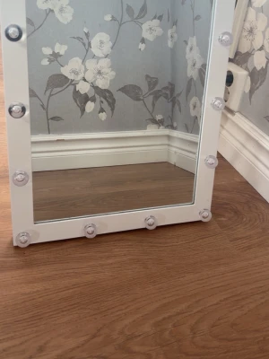 Vit sminkspegel med LED-lampor - Snygg sminkspegel med vit ram och inbyggda LED-lampor runt hela spegeln. Perfekt för att få till rätt ljus när du sminkar dig. Spegeln har en rektangulär form och lamporna ger ett jämnt och klart ljus. Passar perfekt på sminkbordet för en lyxig känsla. Fungerar med batteri och sladd, (sladden e borta)💗 Den e 46cm lång och 36cm bred🫰🏼