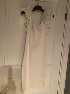 Vit klänning med volangärmar - Supersöt vit klänning med volangärmar och rak passform. Klänningen har en enkel design med fina detaljer på axlarna som ger en romantisk känsla. Perfekt för varma dagar och somriga tillfällen.