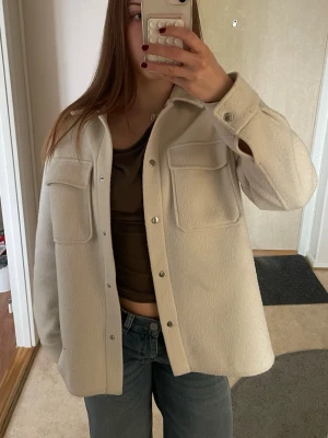 Beige overshirt med fickor Dobber - Säljer en beige overshirt med två stora bröstfickor och knappar framtill. Overshirten har en rak passform och oversized och är gjord i ett mjukt, ull-liknande material. Perfekt att slänga över en t-shirt för en avslappnad look. Använd endast fåtal gånger🤍