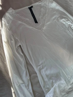 Vit långärmad loungewear-topp spets - Vit långärmad loungewear-topp från Lager 157 med v-ringning och fina spetsdetaljer vid halsringning och ärmslut. Mjuk och skön, perfekt för avslappnade dagar hemma. Materialet känns lätt och följsamt.