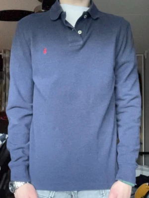 Ralph lauren - Klassisk blå långärmad skjorta från Ralph Lauren med röd broderad logga på bröstet. Perfekt för en stilren och avslappnad look.