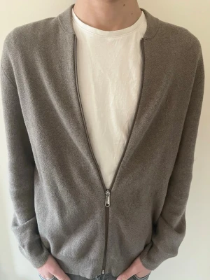 Beige ziptröja från Calvin Klein Jeans - Stilren beige ziptröja från Calvin Klein Jeans i mjukt stickat material. Tröjan är i xs men passar mig som är 177 mycket bra. Tröjan har en smal passform, rund halsringning och dragkedja framtill. Perfekt att bära över en t-shirt för en clean och enkel look.