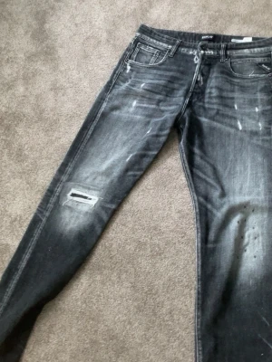 Svarta slitna jeans från Amiri - (Pris kan diskuteras) Säljer ett par svarta jeans från Amiri med skinny fit och slitningar samt färgstänk för en edgy look. Jeansen har klassisk femficksmodell, dragkedjegylf och är tillverkade i denim med stretch. Perfekta för dig som gillar streetwear och vill sticka ut.