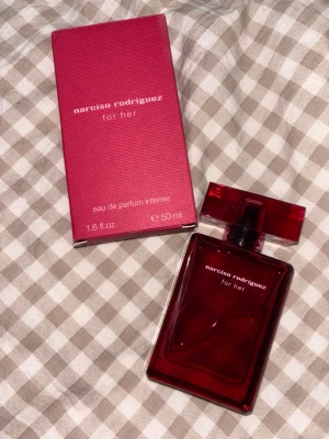 Narciso Rodriguez For Her parfym 50ml - Narciso Rodriguez For Her eau de parfum intense i en snygg, djup röd glasflaska med matchande röd kartong. Flaskan rymmer 50 ml och har en modern, stilren design med rektangulär form och tydlig logga på framsidan.