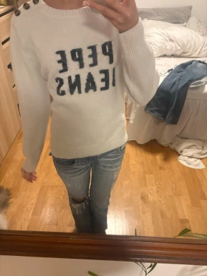 Vit stickad tröja från Pepe Jeans - As snygg bit stickad tröja från Pepe Jeans med svart logotyp framtill. Tröjan har fina dekorativa knappar på ena axeln! Storlek M men passar mig som bär xs, sitter som en xs/s Går ej att köpa längre❤️😊 Pris kan diskuteras vid snabb affär💕