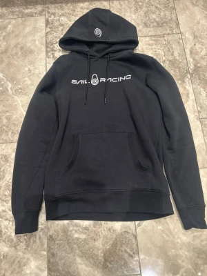 hoodie Sail Racing - Svart hoodie från Sail Racing med vit logga och text på bröstet. Storlek Medium 