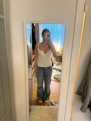 Baggy ljusblå jeans med slitningar - Baggy ljusblå jeans med raka ben och slitna detaljer vid knäna. Jeansen har låg midja och klassisk femficksdesign. Perfekta för en avslappnad och trendig streetstil. Materialet är denim i bomull.