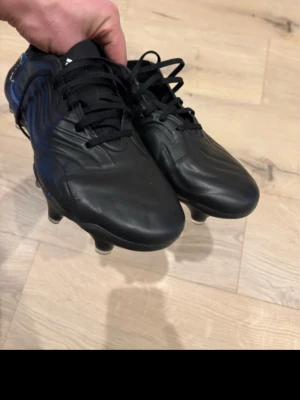 Svarta Adidas Copa fotbollsskor - Säljer ett par helt nya  klassiska svarta Adidas Copa fotbollsskor med snörning och dobbar för gräsplan. Skorna har en stilren design i syntetiskt material och läderlook, perfekta för dig som vill ha bra touch och kontroll på planen.