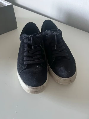 Svarta sneakers från vagabond - Klassiska svarta sneakers från vagabond  med ovandel i mockaimitation och vita, tjocka sulor. Skorna har svarta skosnören och en enkel, stilren design som passar till det mesta. Perfekta för dig som gillar en clean och avslappnad look.