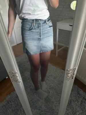 Ljusblå jeanskjol från Levi's - Säljer en ljusblå jeanskjol från Levi's. Kjolen har en rak passform och är i kort modell, perfekt till sommaren. Hög midja på mig med alla knappar knäppta men man behöver absolut inte ha det, jättefint med uppknäppt också. Superskön för att vara en jeanskjol! Inköpt förra sommaren på Carlings för ca 700 kr, använt max 5 gånger och säljer därför nu då den kan bli i mer behov hos någon annan vacker person. Bara att höra av er vid frågor eller andra funderingar